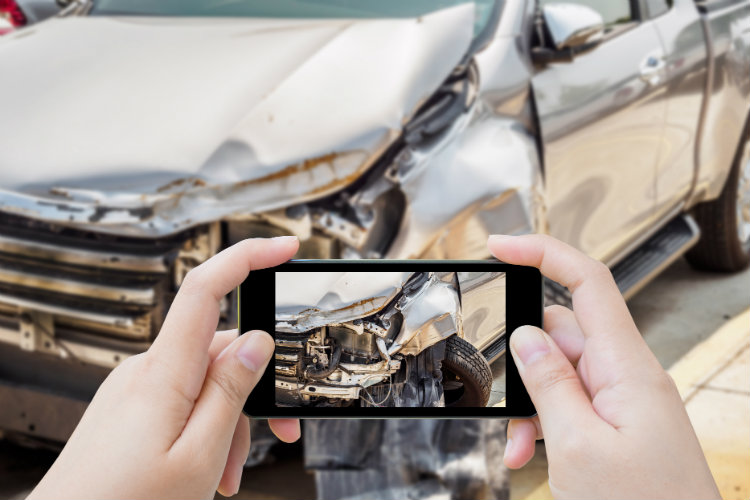 woman using smartphone to take photo of damage after car accident